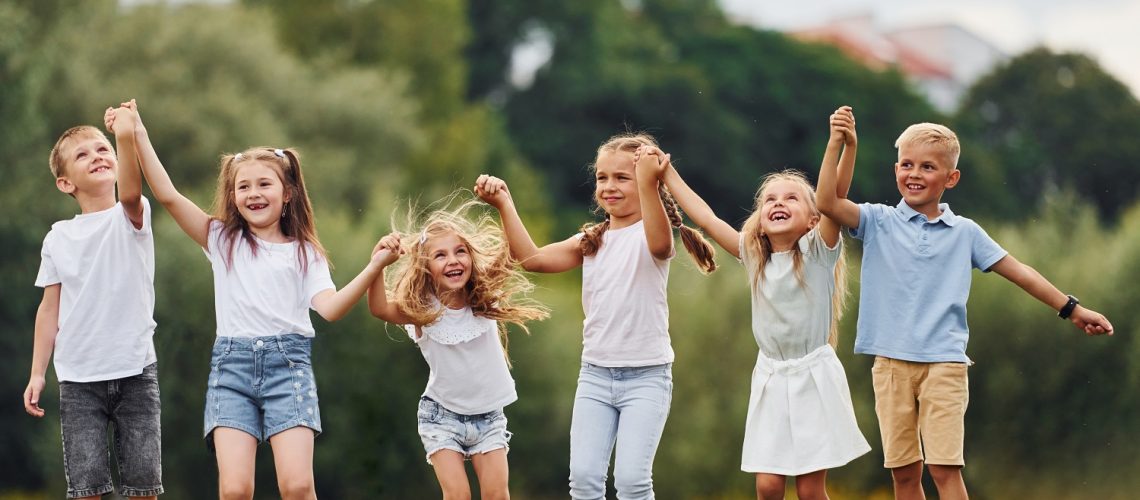Holding each other by hands and jumping. Kids are having fun on the field at daytime together